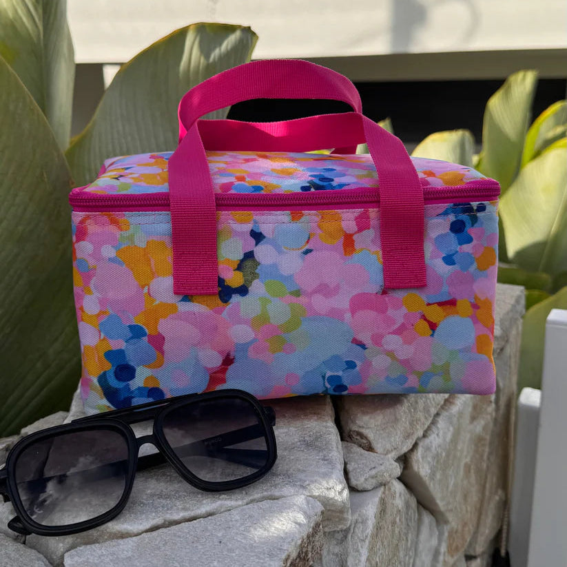 Colorful floral-patterned cooler bag with pink handles on a stone surface, sunglasses nearby.