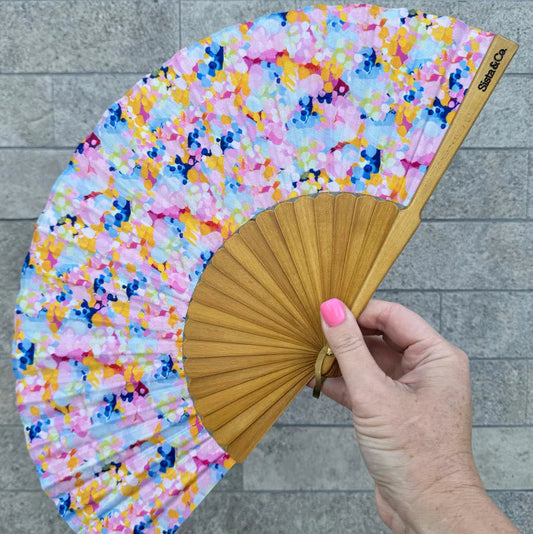 Hand holding a colorful floral fan against a gray tiled background