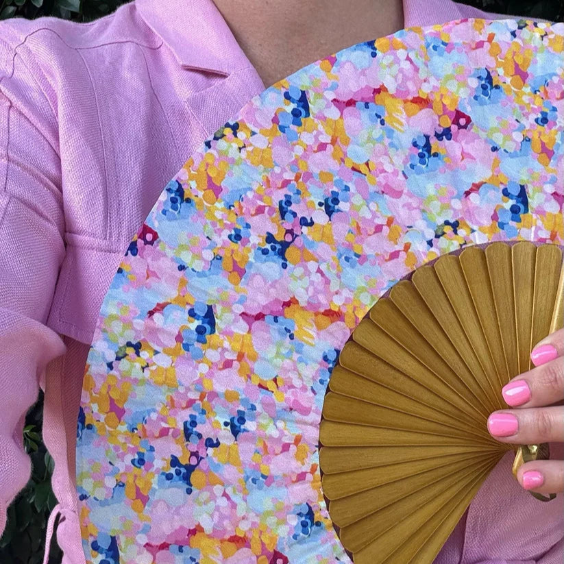 Person holding a colorful floral fan with a pink background