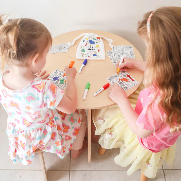 Two young children sitting at a small round table, engaged in an art activity with markers and paper.