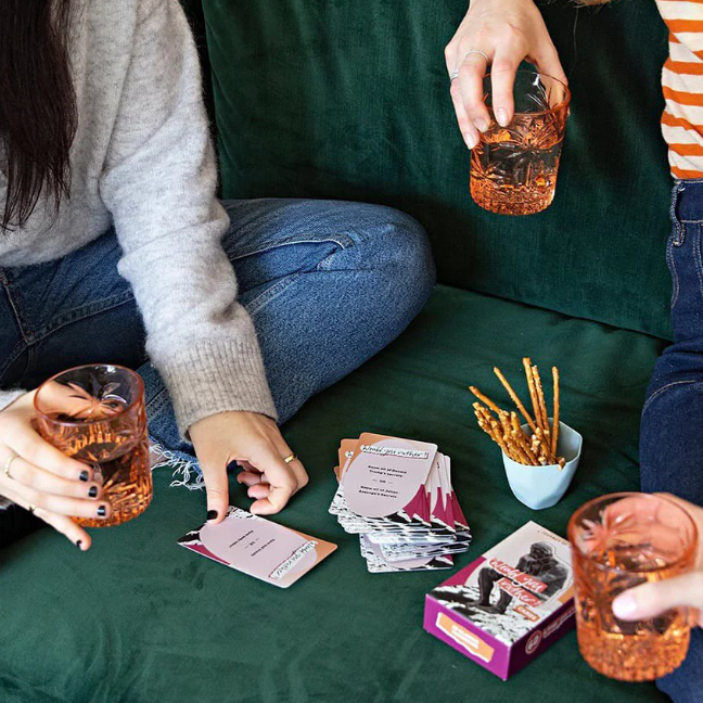 People playing cards on a green couch with drinks and snacks.