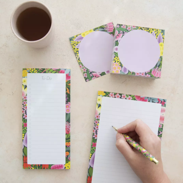 Floral notepads with a hand writing on one of them, next to a cup of coffee.